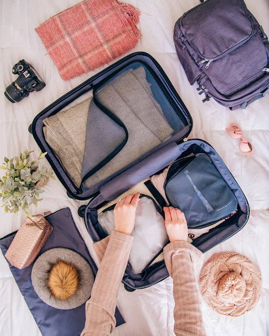Travel toiletry pouch partially open with organized travel essentials arranged beside it on a clean hotel bed surface in natural morning light.